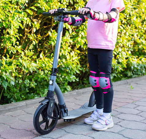 Trottinette avec un enfant portant des protections aux genou, coudes et poignets. 